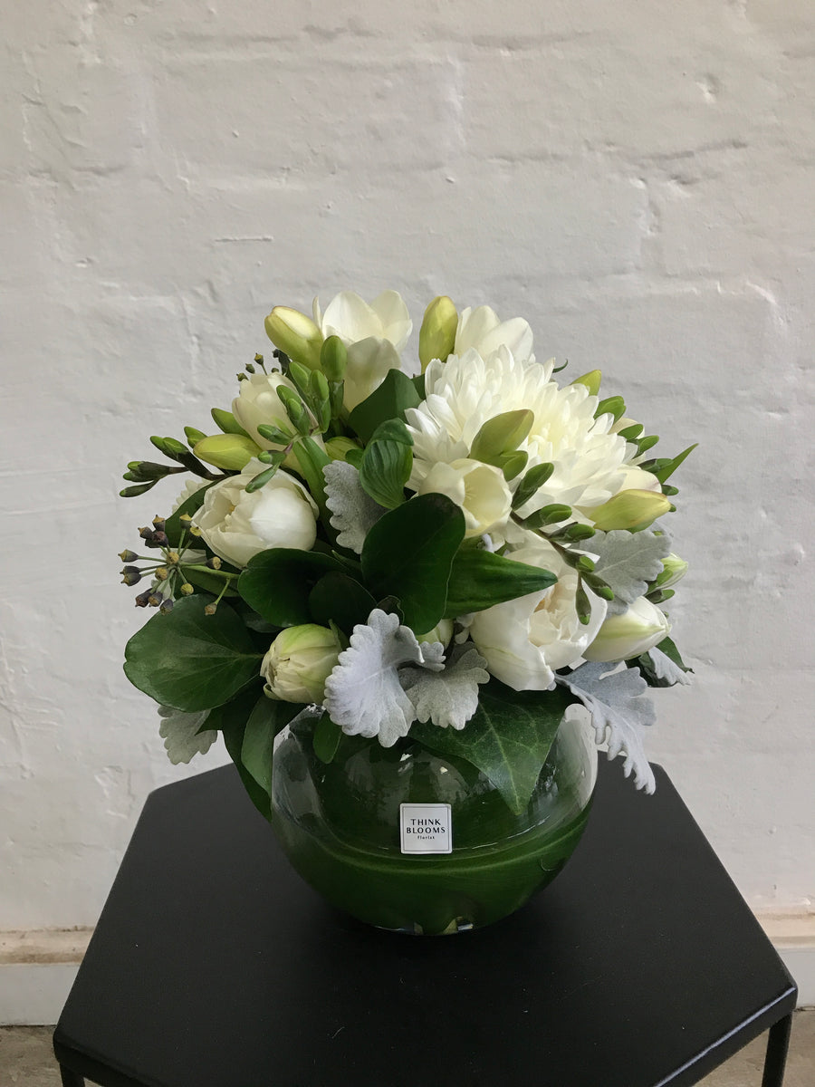 White and green fresh flower arrangement in medium fishbowl vase with white roses, white chrysanthmum, white freesia and other seasonal fresh flowers